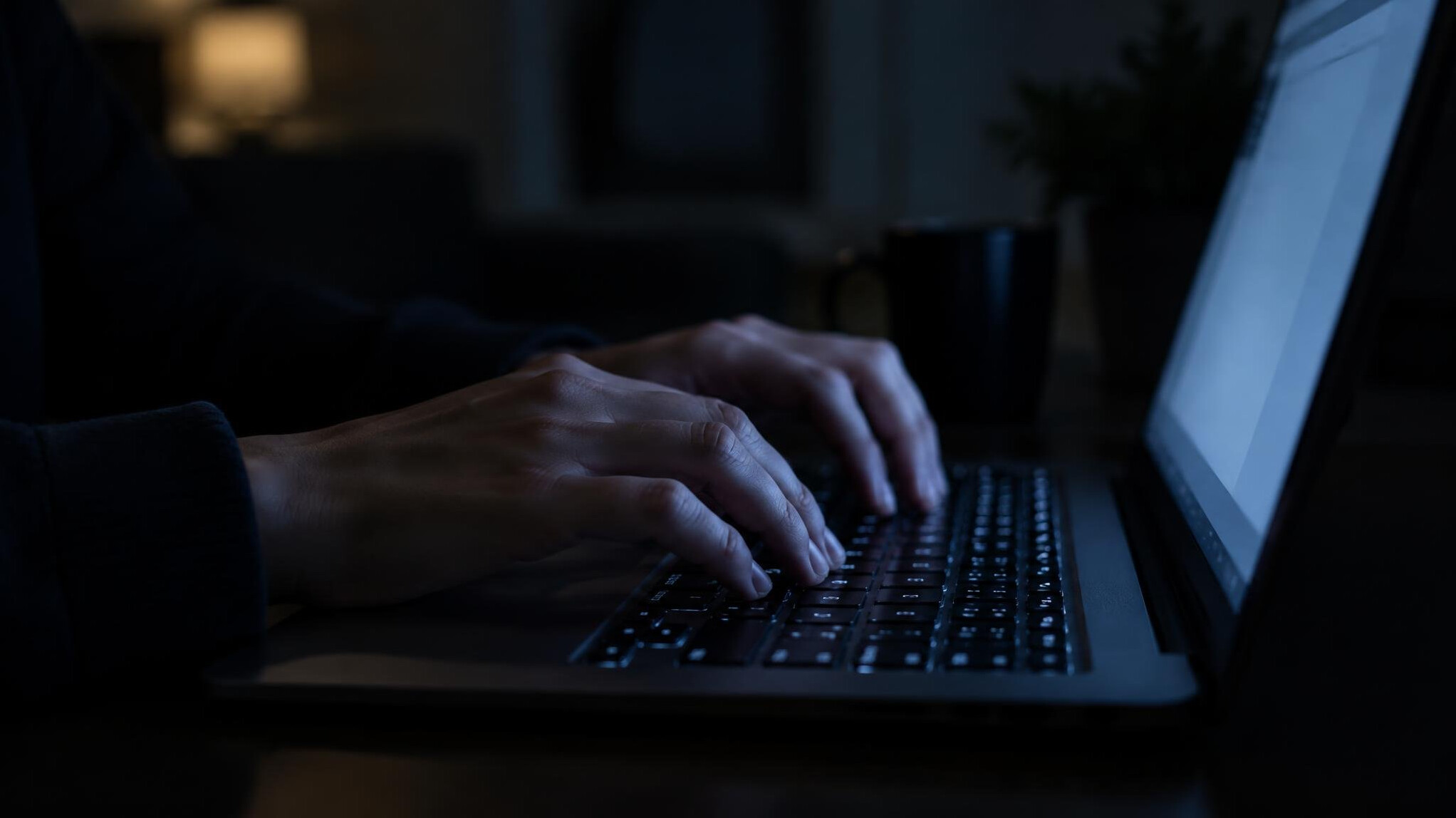 Hands typing on a laptop in a dimly lit room